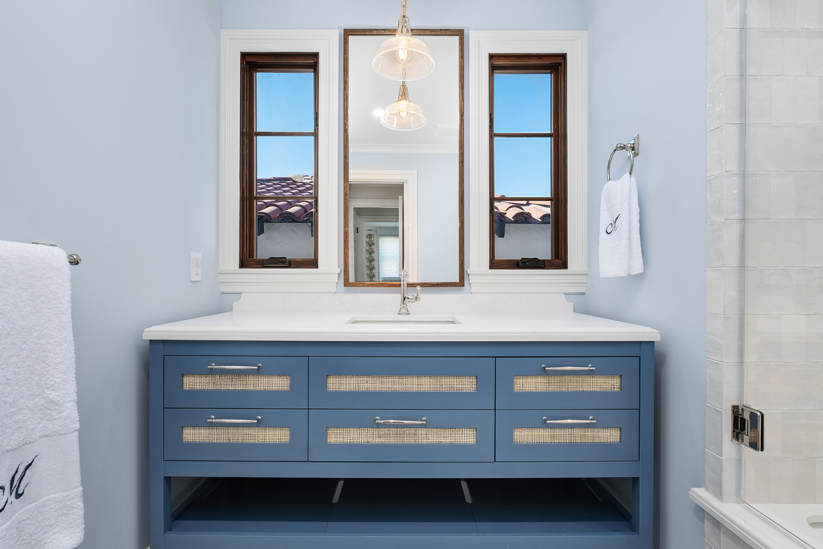 Cane-front navy vanity with quartz top and antique-brass mirror